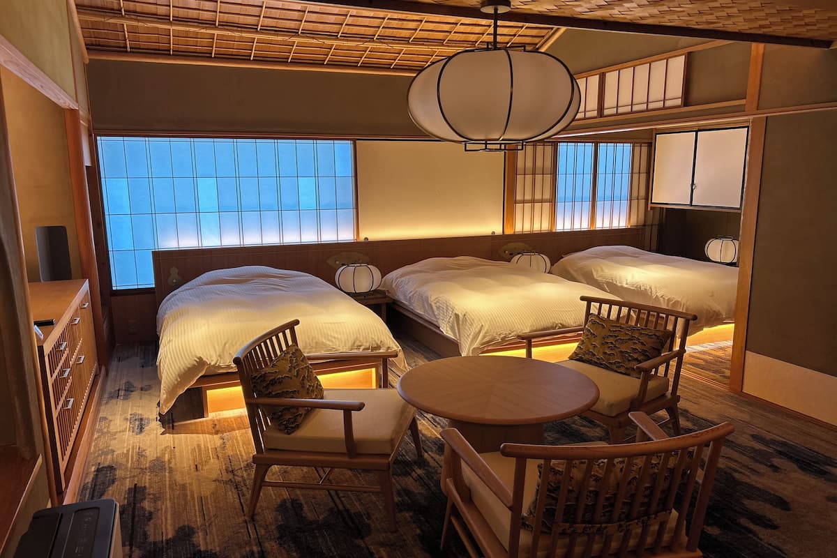 Ein traditioneller japanischer Raum mit zwei Betten, einem hölzernen Stuhl, einem kleinen Tisch und einem großen Fenster mit Aussicht.