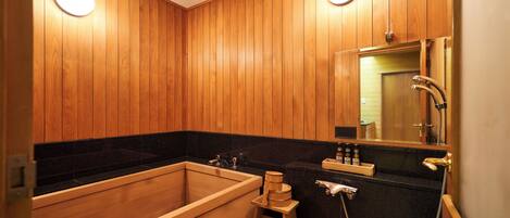 A wooden-paneled bathroom with a bathtub, a small wooden stool, a sink, and a mirror.