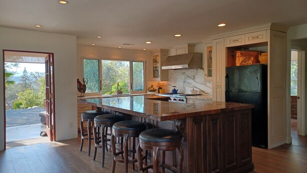 A modern kitchen with a large island, bar stools, a black refrigerator, and a view of the outdoors. - Pets Welcome <br>Private Home on 2 Acres<br>Hiking, biking, Trails <br> (Altadena)