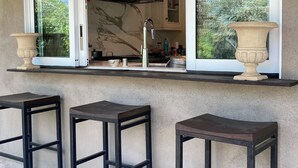 An outdoor kitchen with a large window, a stainless steel range hood, and three black bar stools. - Pets Welcome <br>Private Home on 2 Acres<br>Hiking, biking, Trails <br> (Altadena)