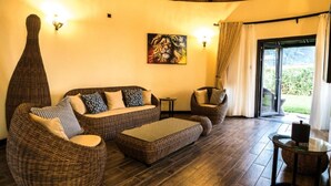 A cozy lounge area with wicker furniture, a painting on the wall, and a view through the glass door. - Hunters Paradise Cottages (Bungoma)