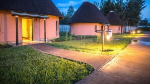 A row of thatched-roof cottages with a paved walkway in between. - Hunters Paradise Cottages (Bungoma)