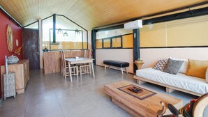 Ein geräumiger Wohnbereich mit Holzbalkendecke, einer Couch, einem Esstisch mit Stühlen und einer Küchenzeile im Hintergrund.