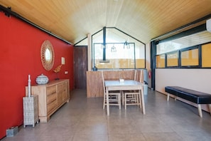 A spacious room with a high ceiling, a wooden bench, a dining table with chairs, and a red wall with a decorative mirror. - Villa Bima II (Nusa Dua)