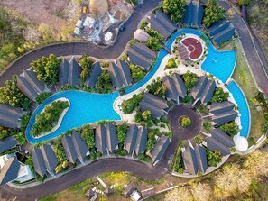 An aerial view of a residential area with a central swimming pool, surrounded by houses with sloped roofs. - Villa Bima II (Nusa Dua)