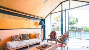 Ein Zimmer mit Holzboden, einem Sofa mit gemusterten Kissen, einem Holztisch und zwei Stühlen mit gestreiften Kissen.