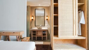 Ein Hotelzimmer mit einem Holzbüro, einem Schminktisch aus Holz mit Spiegel, einem Bett und einem Holzschrank mit aufgehängtem Handtuch.