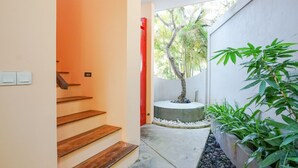 Eine schmale Treppe führt zu einer Tür, ein kleiner Baum in einem Kübel, und eine Wand mit einer roter Tür.