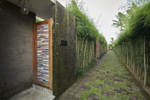 Stroll through lush bamboo and tropical foliage to a serene entrance, flanked by a traditional wooden door and a textured facade.
