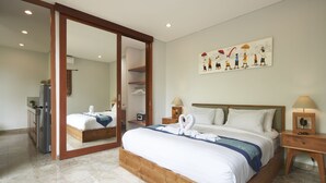 A bedroom with a large bed, a wardrobe, a mirror, a painting, and a nightstand with a lamp. - Prema Uja Villas (Ubud)