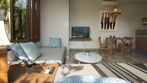 A modern living room with a sofa, coffee table, and TV. There is a dining area with a table and chairs. - Prema Uja Villas (Ubud)