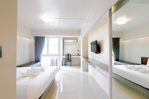 Una habitación de hotel con dos camas, televisión, espejo y ventana con cortinas.
