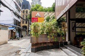 Un edificio con un cartel en forma de A, una jardinera de ladrillo con bambú y una fachada con toldo azul.