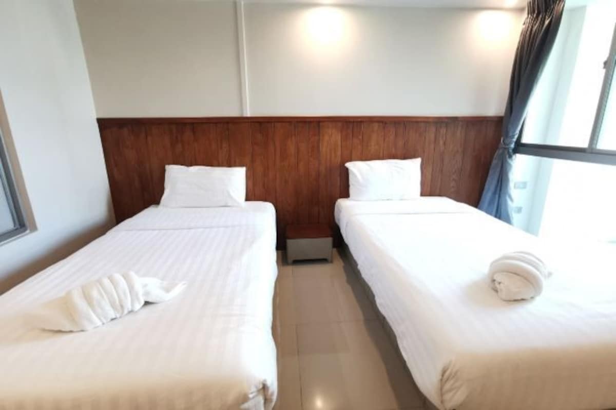 Ett hotellrum med två separata sängar, en sänggavel i trä, vita sängkläder och ett fönster med gardiner.