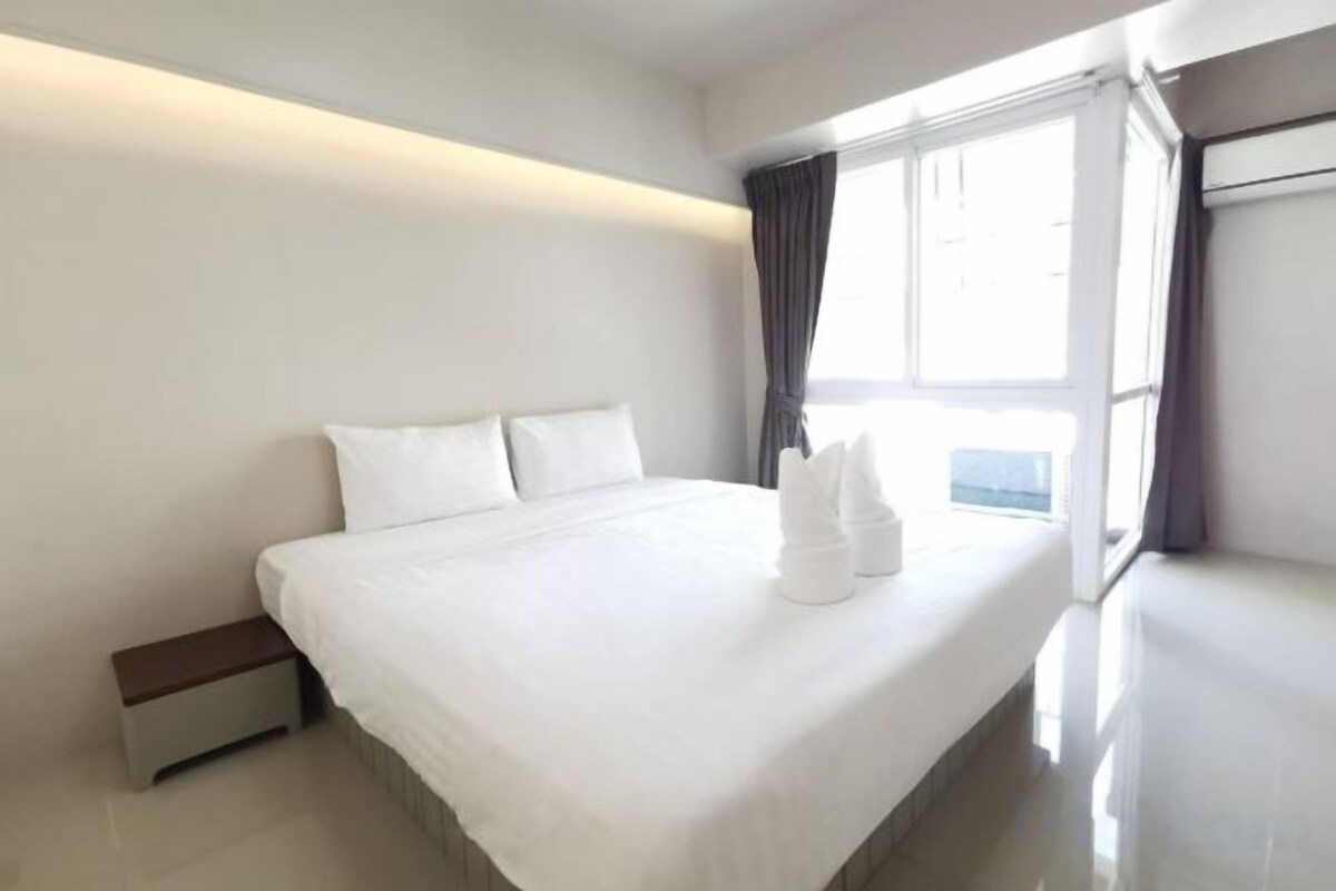A hotel room with a large bed, a bedside table, and a window with curtains.
