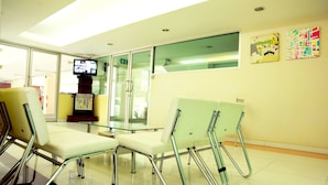 A waiting area with chairs and a glass table, a television on a stand, and a wall with framed pictures. - Meesook Residence (Nonthaburi)
