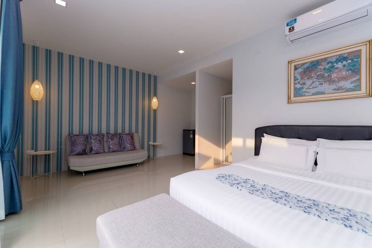 A modern hotel room with a large bed, a sofa, and a dining table.