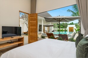 A bedroom with a TV, a large bed, and a view of an outdoor pool area. - Lespalm Taraburi Pool Villa (Si Sunthon)