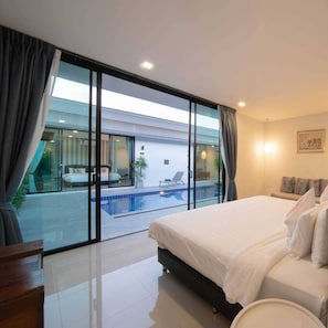 A modern hotel room with a large bed, a view of a swimming pool, and a balcony with curtains. - Lespalm Taraburi Pool Villa (Si Sunthon)