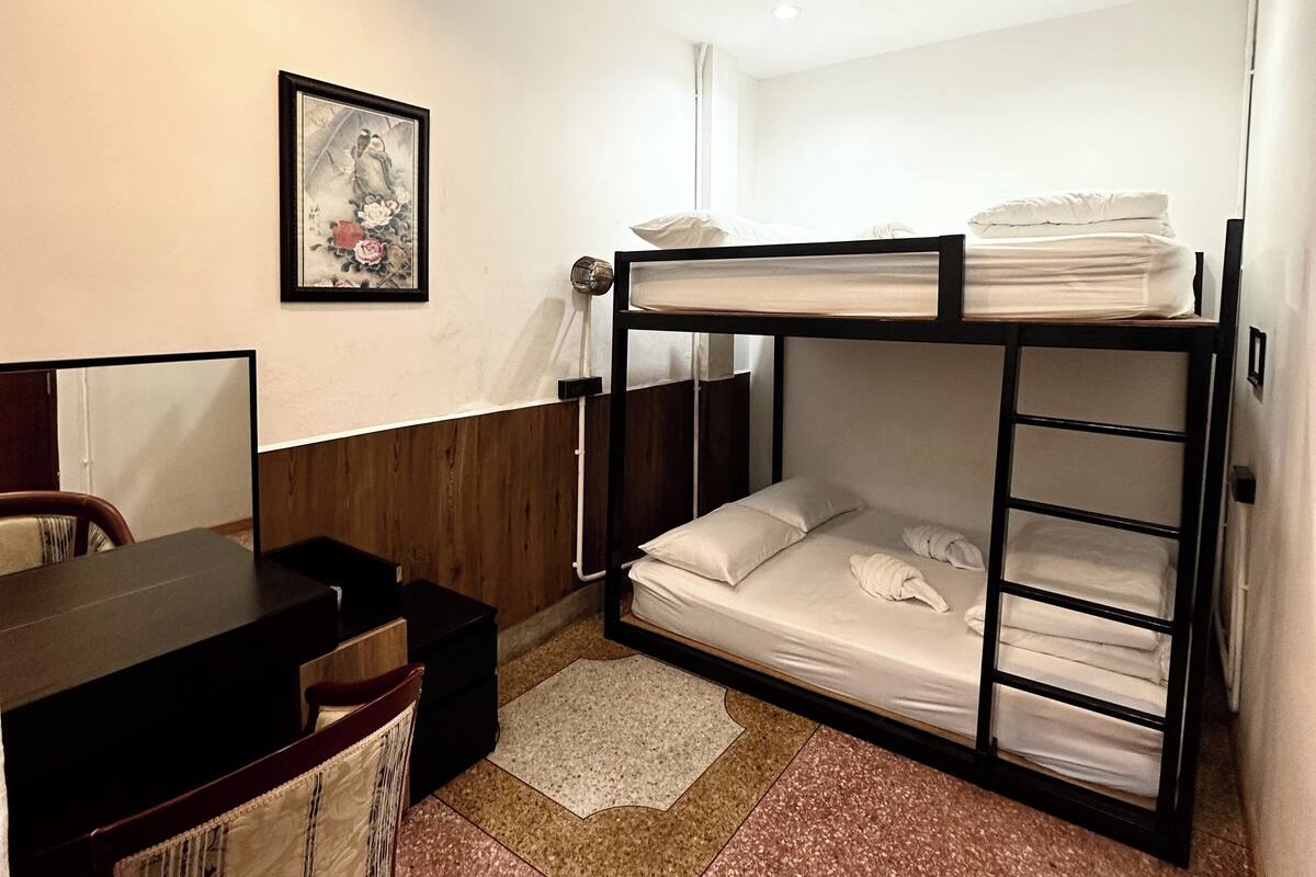 A bunk bed room with a desk and chair, a framed picture on the wall, and a small rug on the floor.