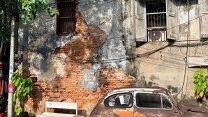 Pared de ladrillo desgastada con un banco y un coche estacionado adelante.