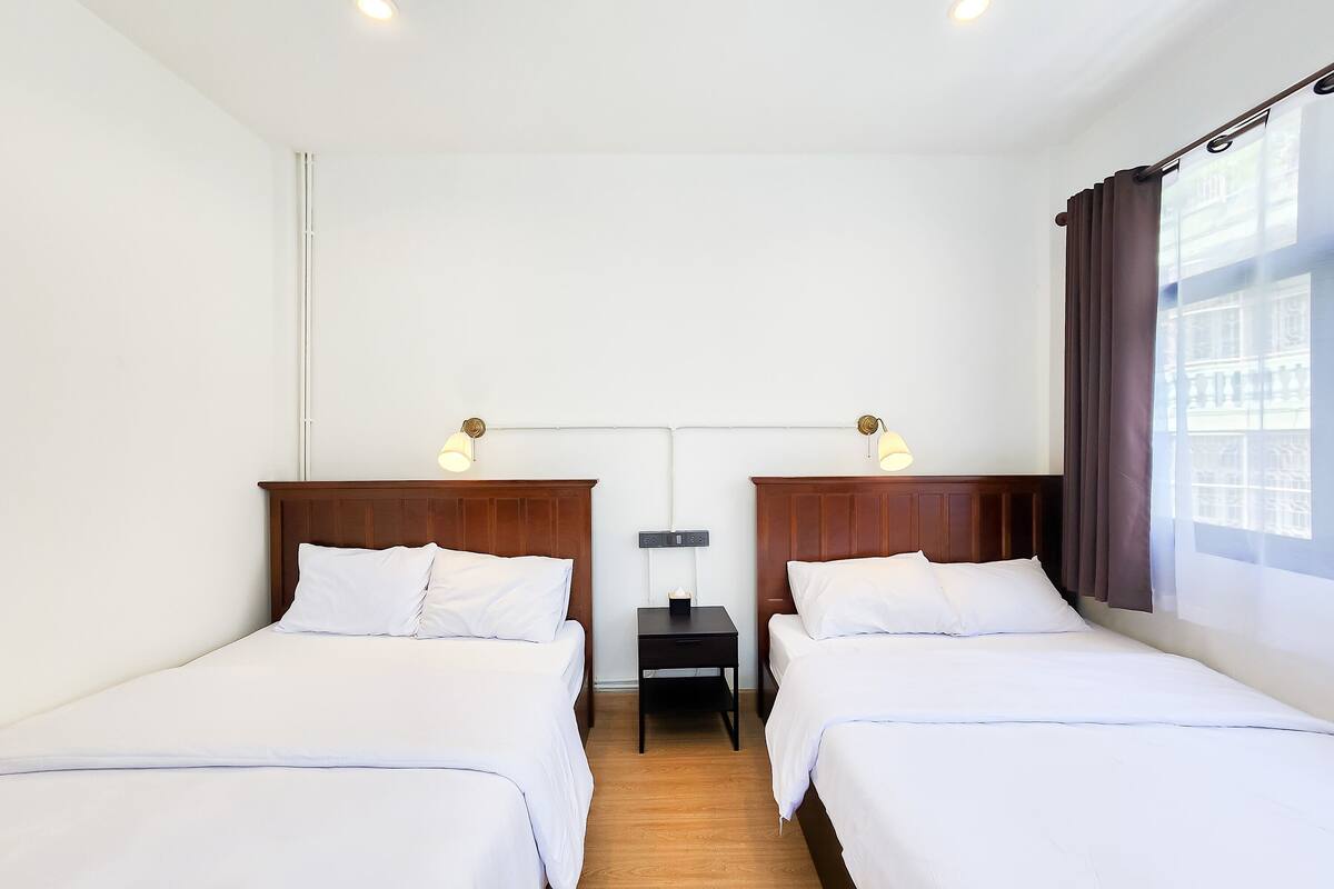 A hotel room with two beds, a nightstand, and a window with curtains.
