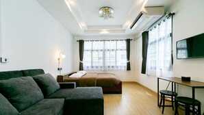 Una habitación moderna con sofá, cama, escritorio con sillas y televisor en la pared.