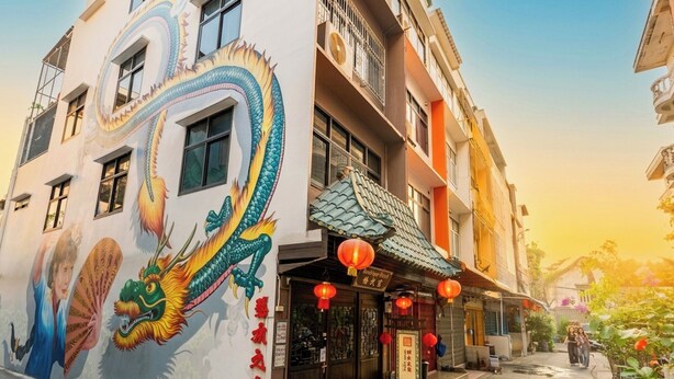 Un edificio con un mural de un dragón colorido, la entrada de un restaurante chino tradicional y un cielo despejado.