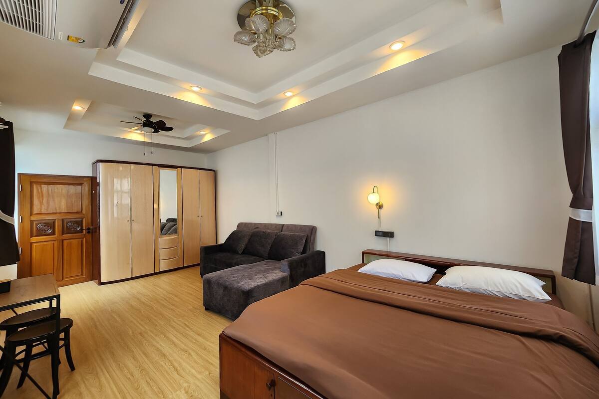A bedroom with a bed, a sofa, a desk, and a wardrobe.
