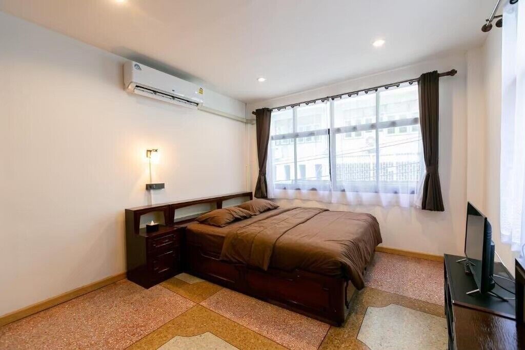 Ein Schlafzimmer mit einem Bett, einem Nachttisch mit Lampe, einer Klimaanlage und einem Fenster mit Vorhängen.