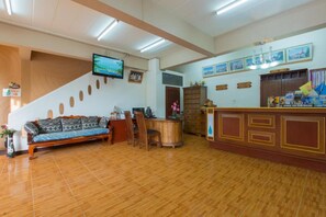 A hotel lobby with a wooden floor, a sofa, a reception desk, and a television mounted on the wall. - Patong Rai Rom Yen Resort SHA (Patong)