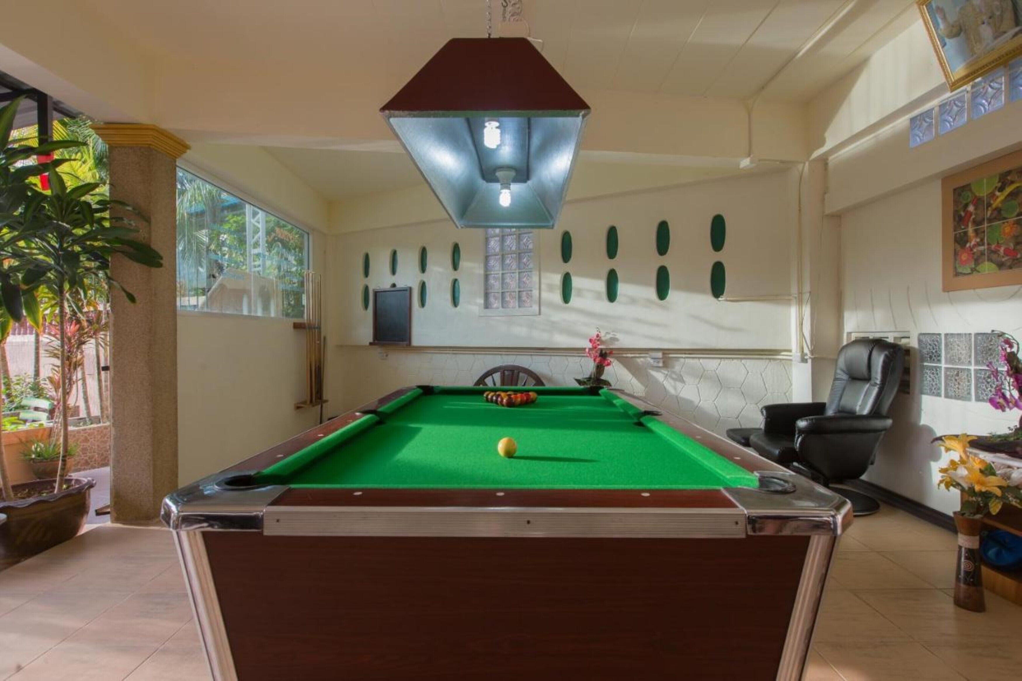 A pool table in a room with a large window, a ceiling light, and a chair.