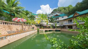 A hotel with a pool, palm trees, and a bridge. - Patong Rai Rom Yen Resort SHA (Patong)