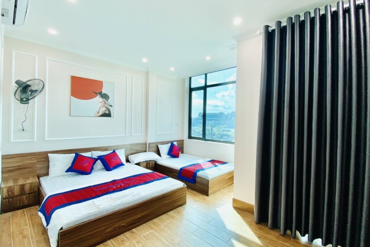Quarto de hotel com duas camas, uma janela grande, um ventilador e um quadro na parede.