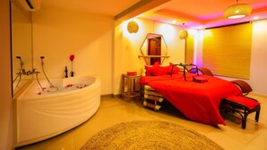 A bedroom with a large bathtub, a bed with red bedding, and a small table with a red bowl. - Long Den Do Hotel (Ho Chi Minh City)