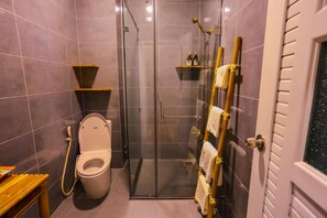 A modern bathroom with a glass-enclosed shower, a toilet, and a shelf with toiletries. - Long Den Do Hotel (Ho Chi Minh City)