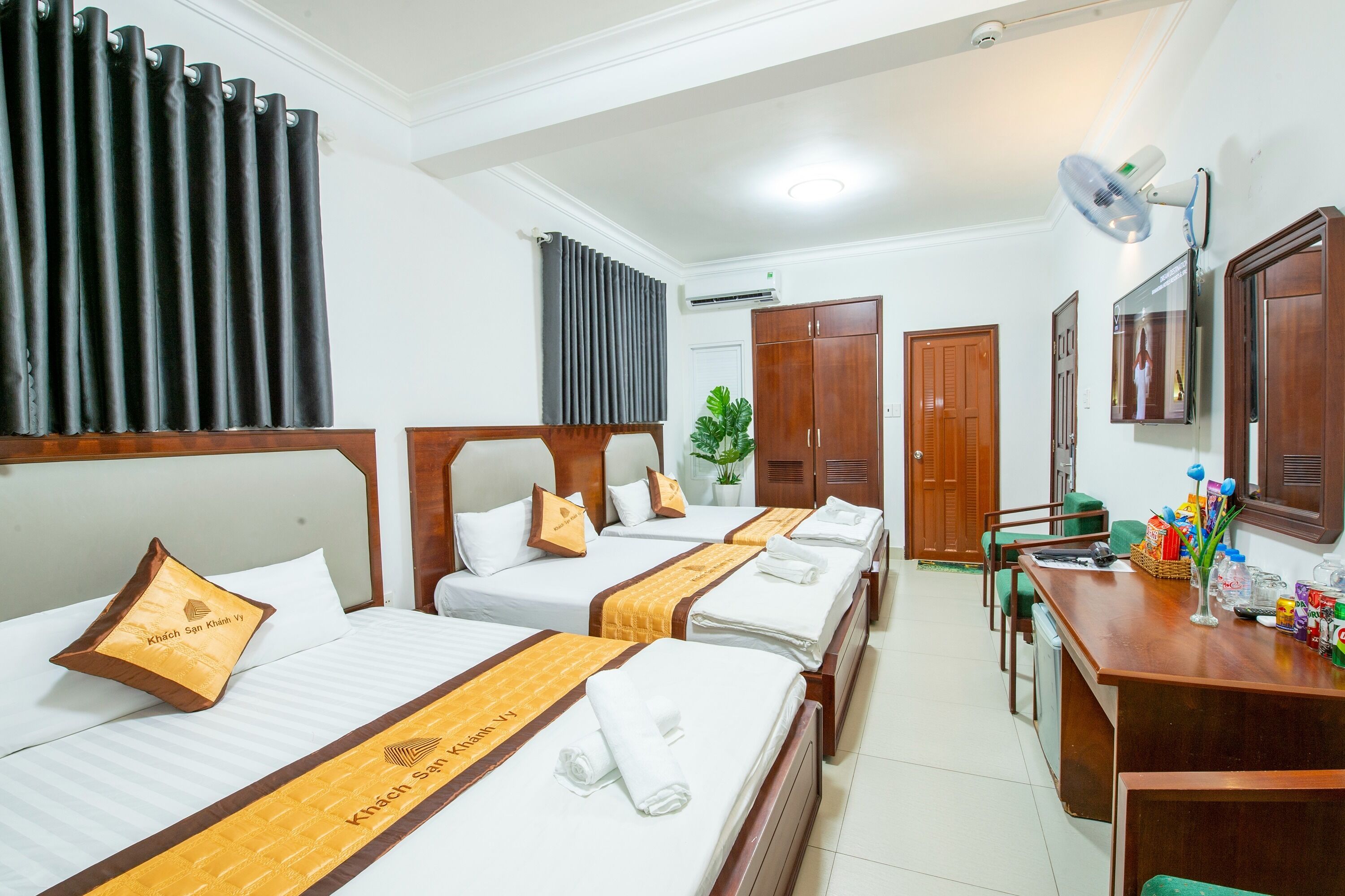 A hotel room with four beds, a desk with a fan, and a mirror.