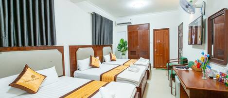 A hotel room with four beds, a desk with a fan, and a mirror.