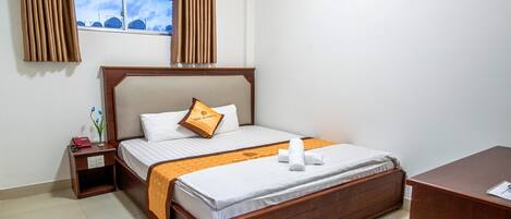Habitación de hotel con cama de madera, mesita de noche, escritorio y ventana con cortinas.