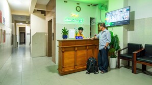 A hotel reception desk with a neon sign, a clock, and a TV displaying multiple rooms. - Khanh Vy Hotel (Ho Chi Minh City)