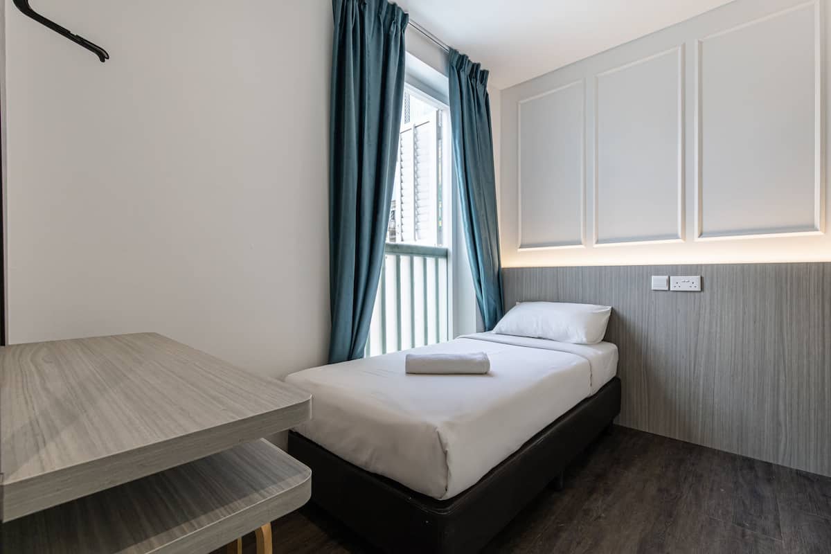 A small, neatly arranged bedroom with a bed, a bedside table, and a window with curtains.