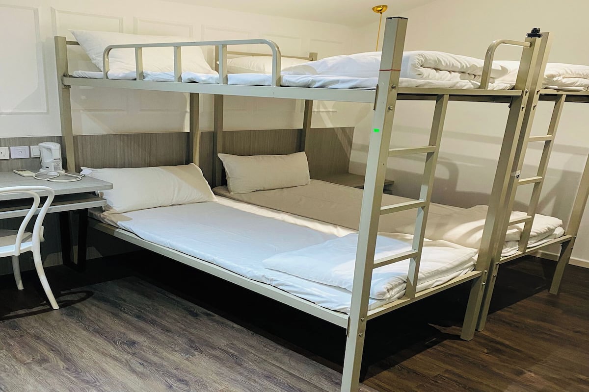A bunk bed room with a desk and chair, a power outlet, and a wooden floor.