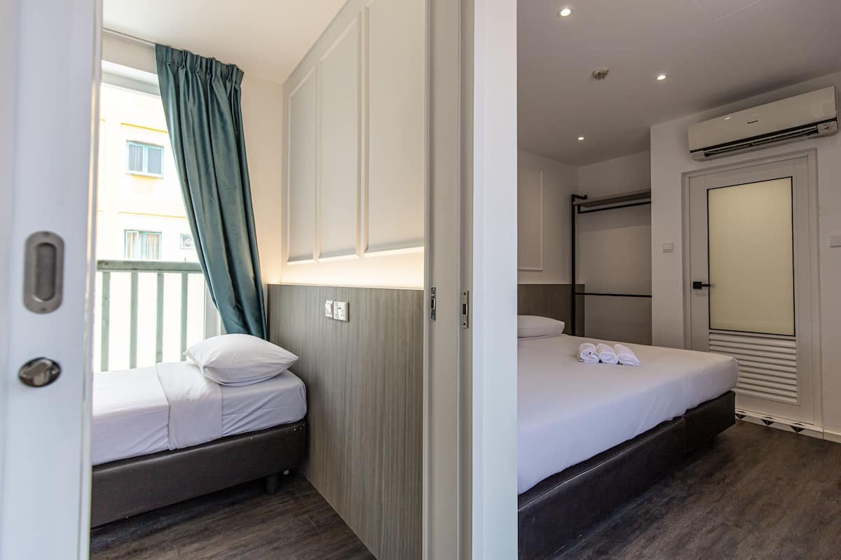 A hotel room with a bed, a wardrobe, a window with curtains, and an air conditioning unit.