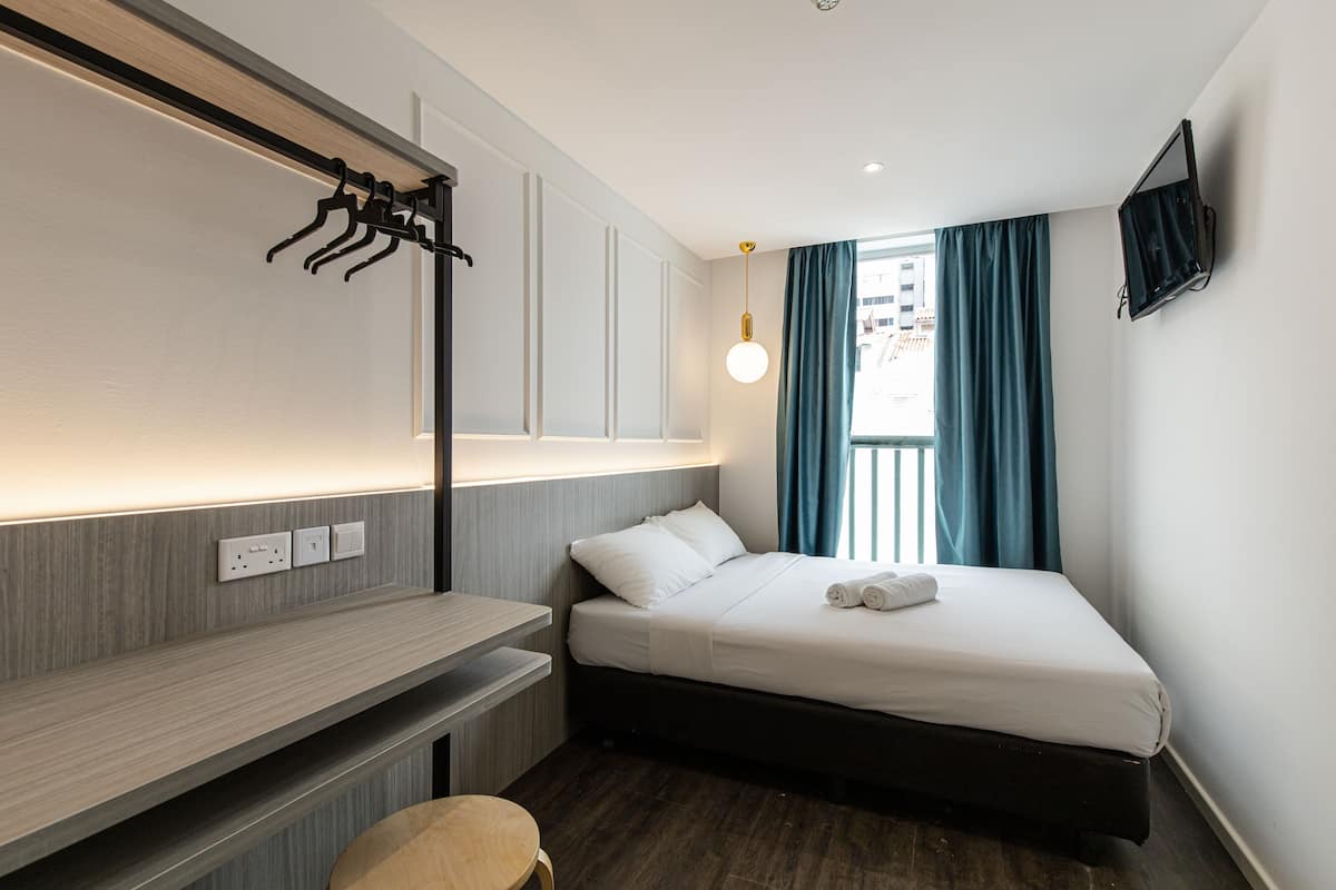 A modern hotel room with a bed, bedside table, and a desk.