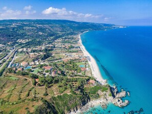 An aerial view of a coastal town with a long beach, residential areas, and a mix of natural and developed landscapes.