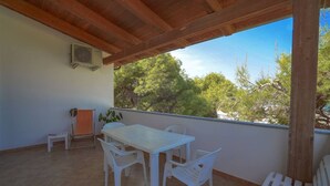 A covered patio with a white table and chairs, an air conditioning unit, and a view of trees. - Residence Emmesse Trilocal 3 Rooms (Zambrone)