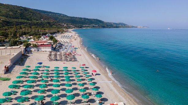 A beach with rows of umbrellas and sun loungers, a clear blue sea, and a hilly landscape in the background. - Residence Emmesse Trilocal Apartment 3 Rooms (Zambrone)