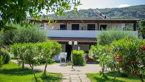 A two-story building with a tiled roof, surrounded by lush greenery and flowering plants. - Residence Emmesse Trilocal Apartment 3 Rooms (Zambrone)