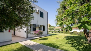 A modern white building with air conditioning units, a small garden with a tree and a flower bush, and a paved pathway leading to the entrance. - Residence Emmesse Appartamenti Stardard (Zambrone)