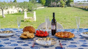 A table set outdoors with a bottle of wine, glasses, bread, tomatoes, and a pizza.